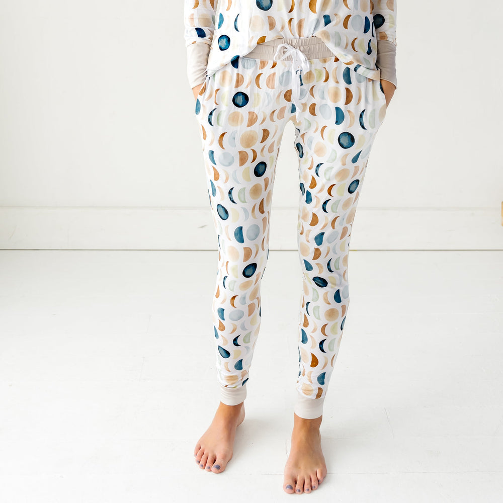 Cropped image of a woman wearing Luna Neutral printed pajama pants and matching long sleeve pajama top. This print features phases of the moon in the sweetest shades of creams, tans, and navy watercolor in an all over repeat pattern.
