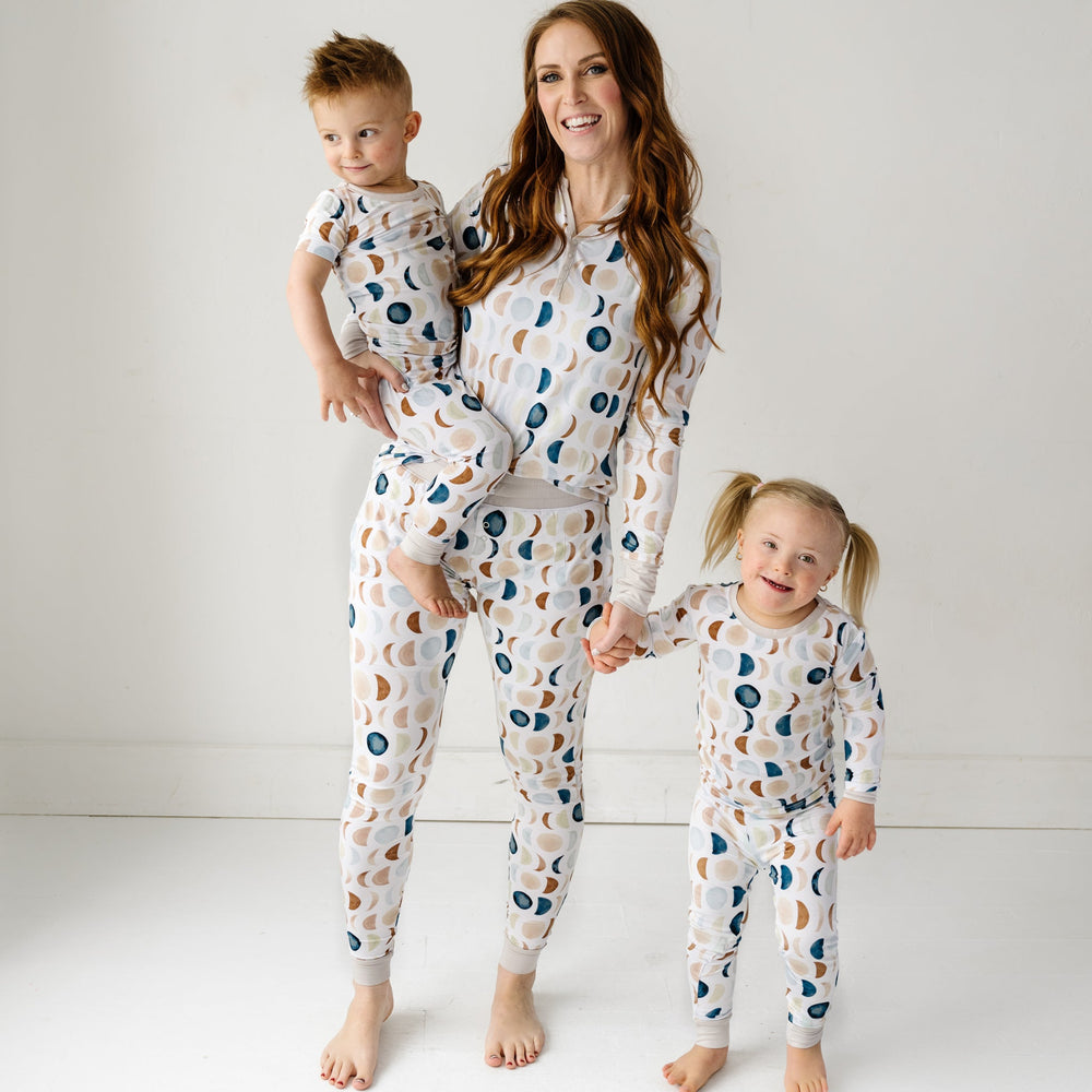 Image of a mother and two young children in matching pajama sets in Luna Neutral print. This print features phases of the moon in the sweetest shades of creams, tans, and navy watercolor in an all over repeat pattern.