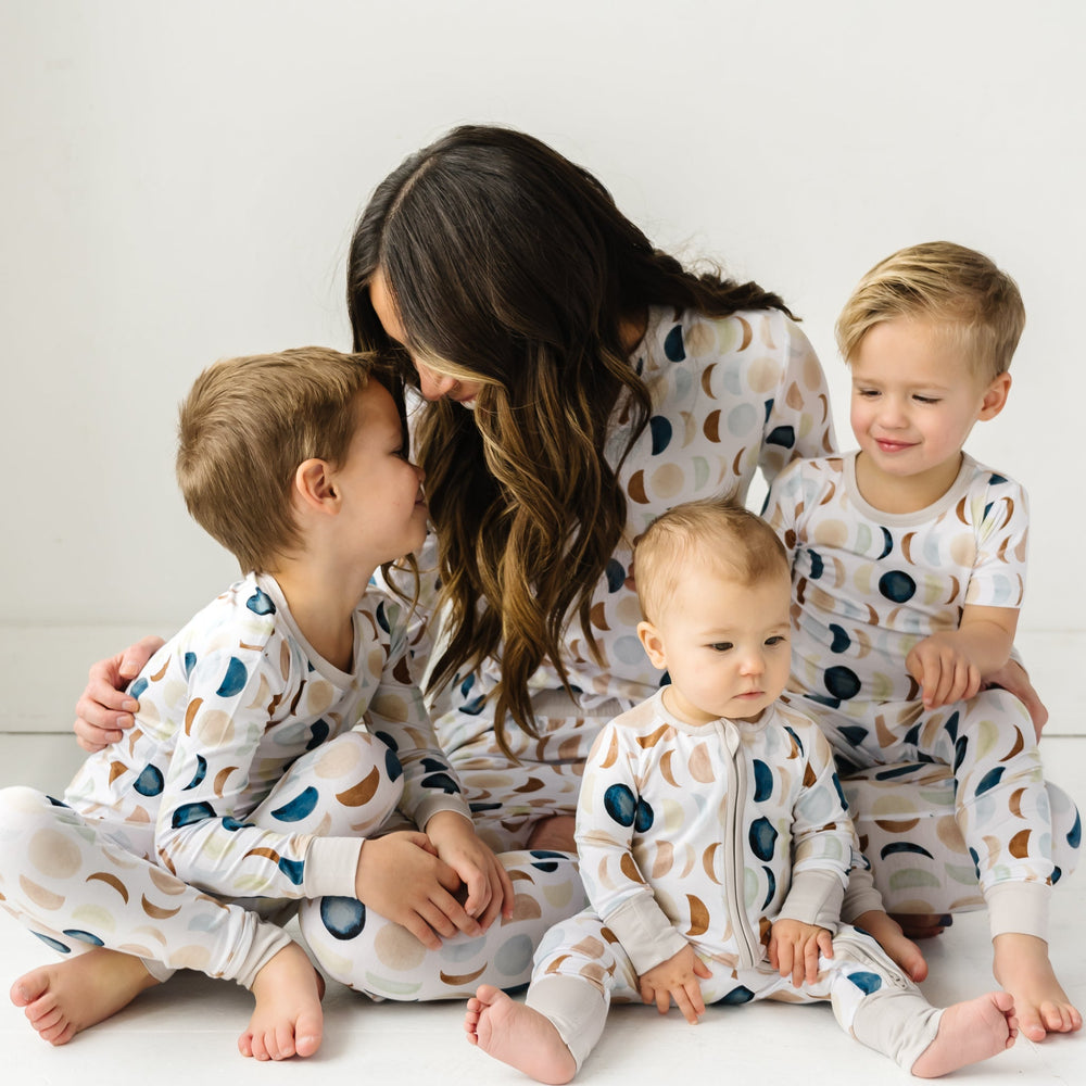 Image of a mother and three young children in matching pajama sets in Luna Neutral print. This print features phases of the moon in the sweetest shades of creams, tans, and navy watercolor in an all over repeat pattern.