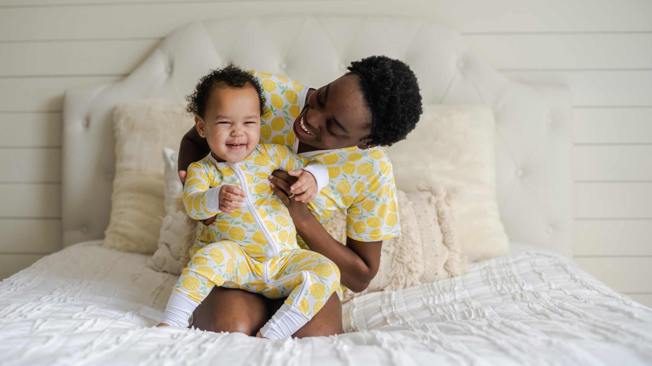 toddler and mom sitting on bed in matching lemon zipper pajamas 