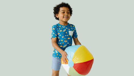 child wearing little sleepies play clothes and holding a beach ball