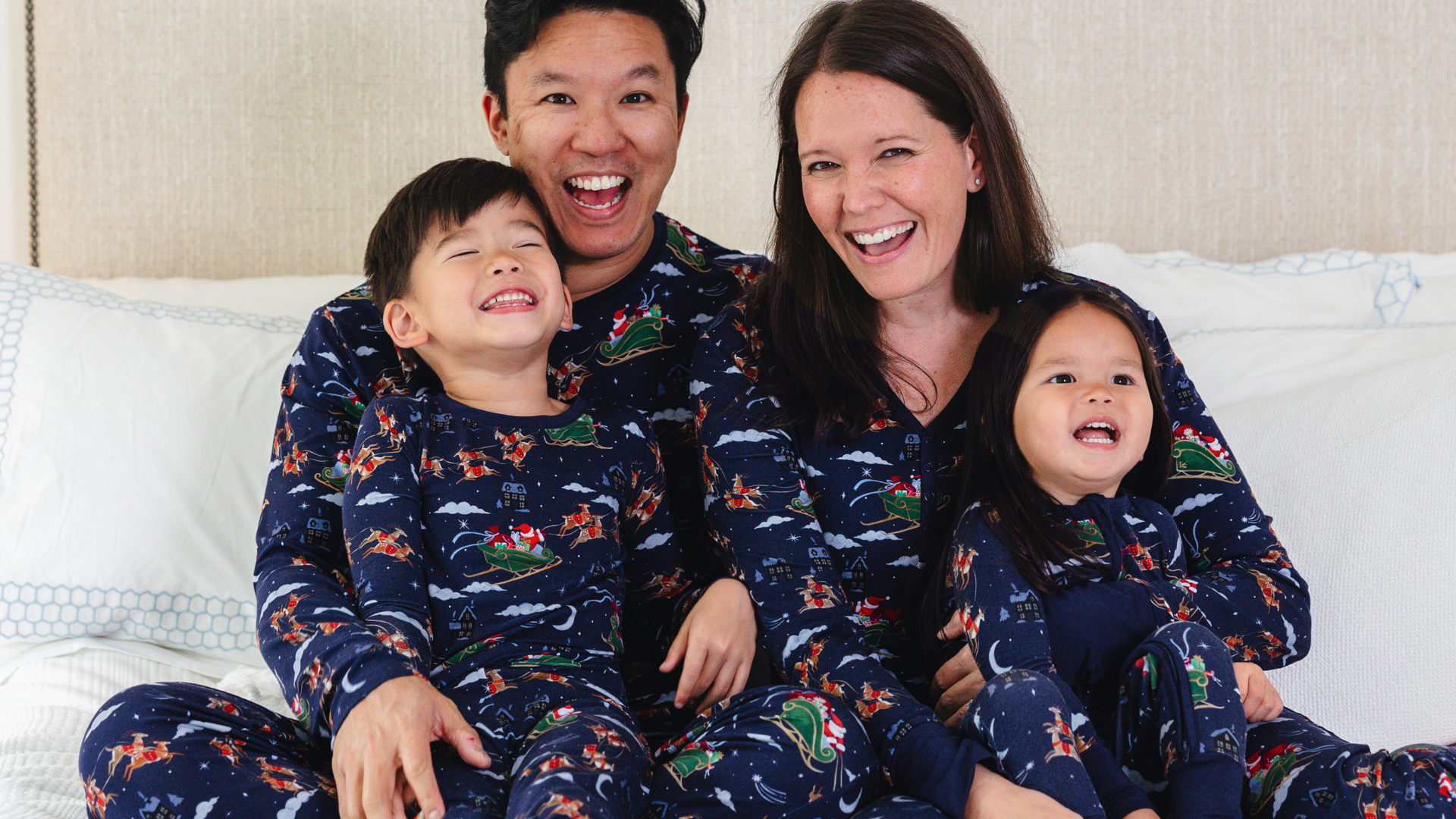 two little girls in pink pajamas with christmas trees on them sitting on a bed with their mom