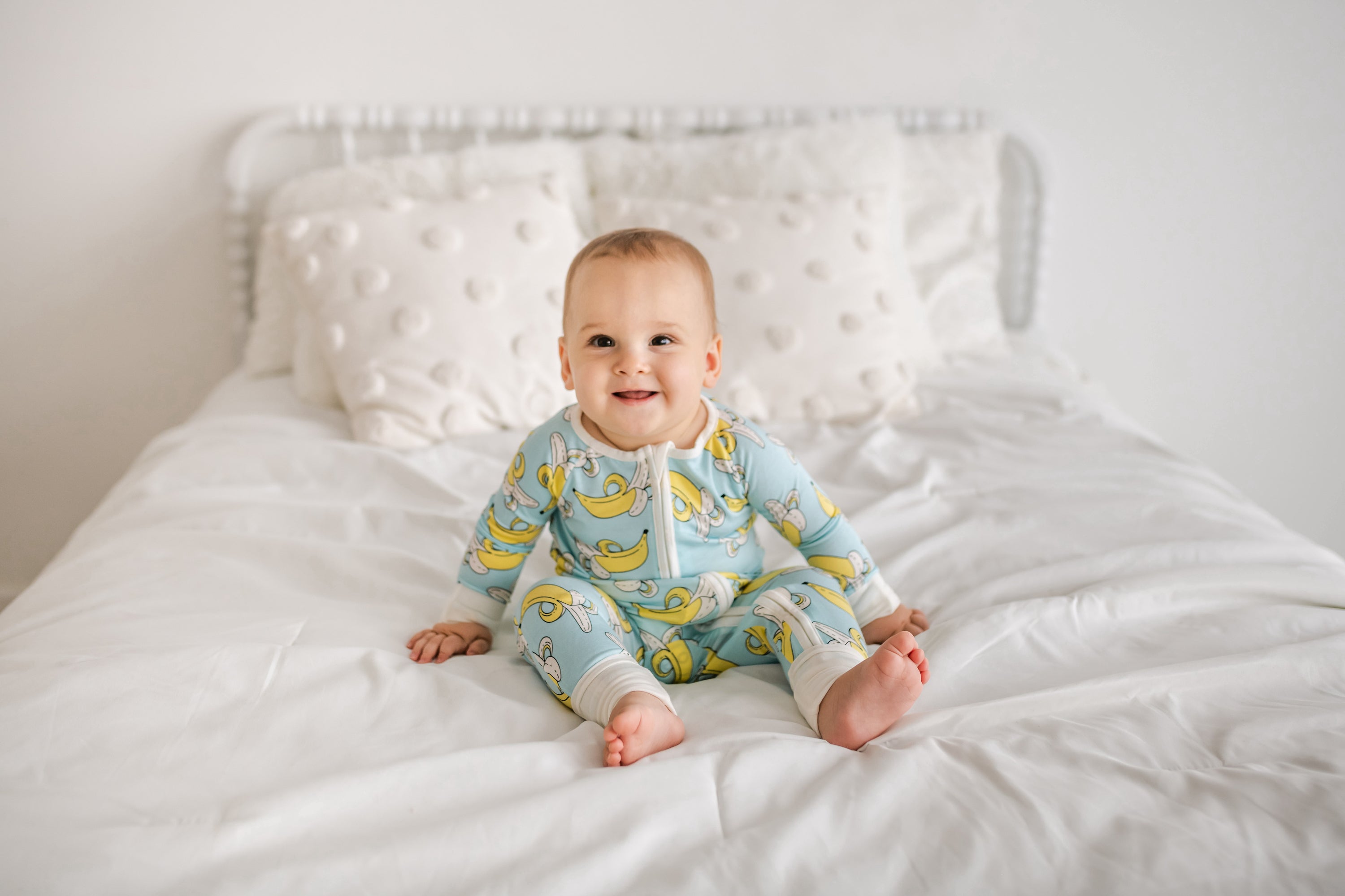 baby in banana pajamas sitting on a bed