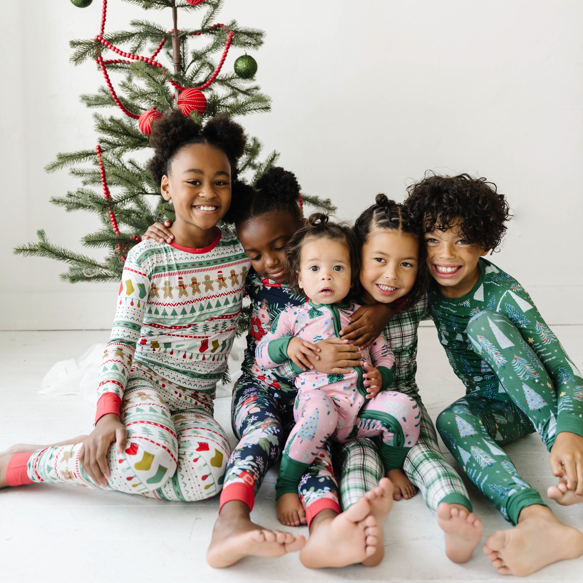 group of five children sitting in front of a christmas tree in coordinating holiday pajamas