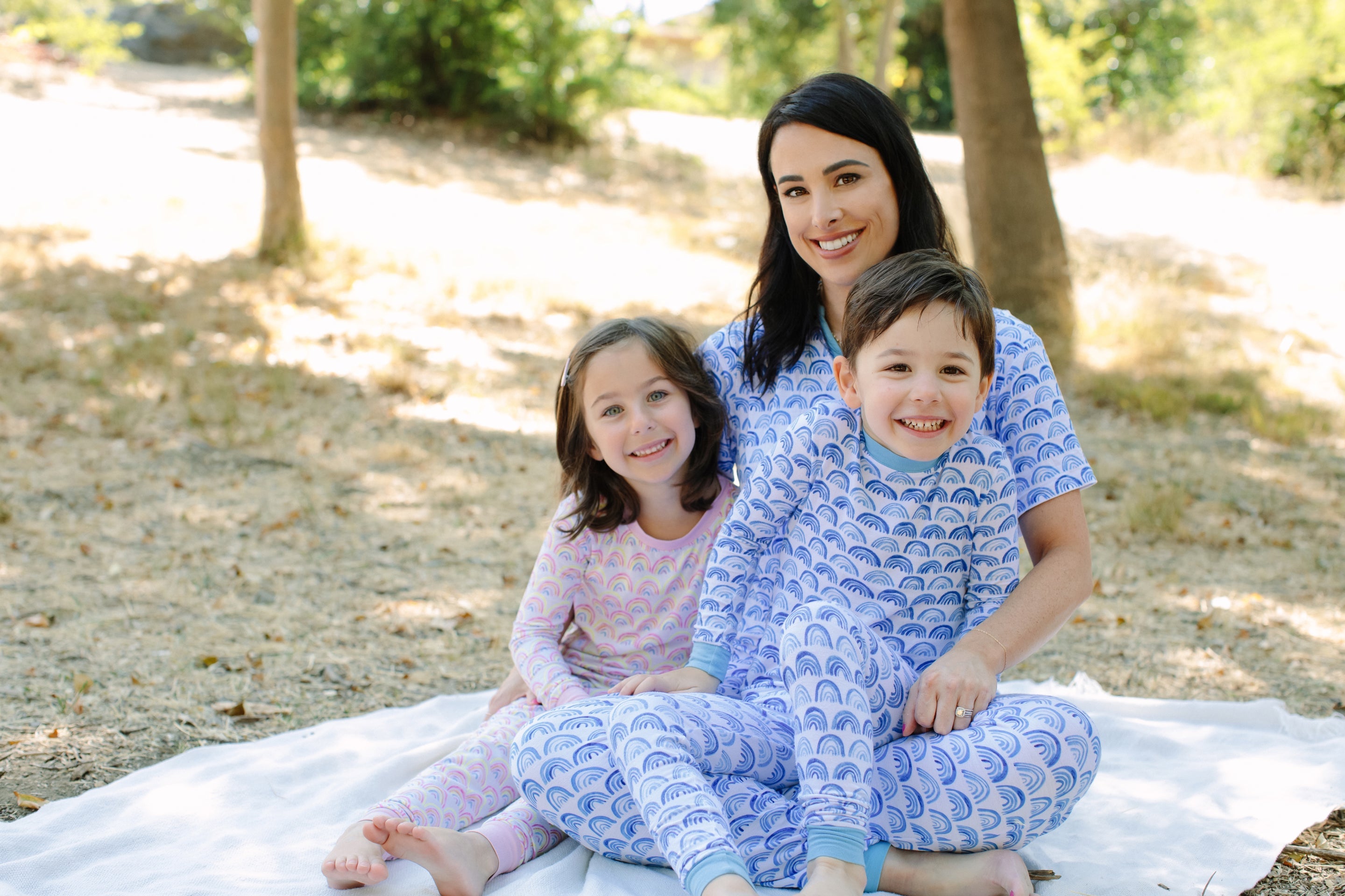 Image of Maradith and her two children sitting on a blanket wearing matching Rainbow pajamas