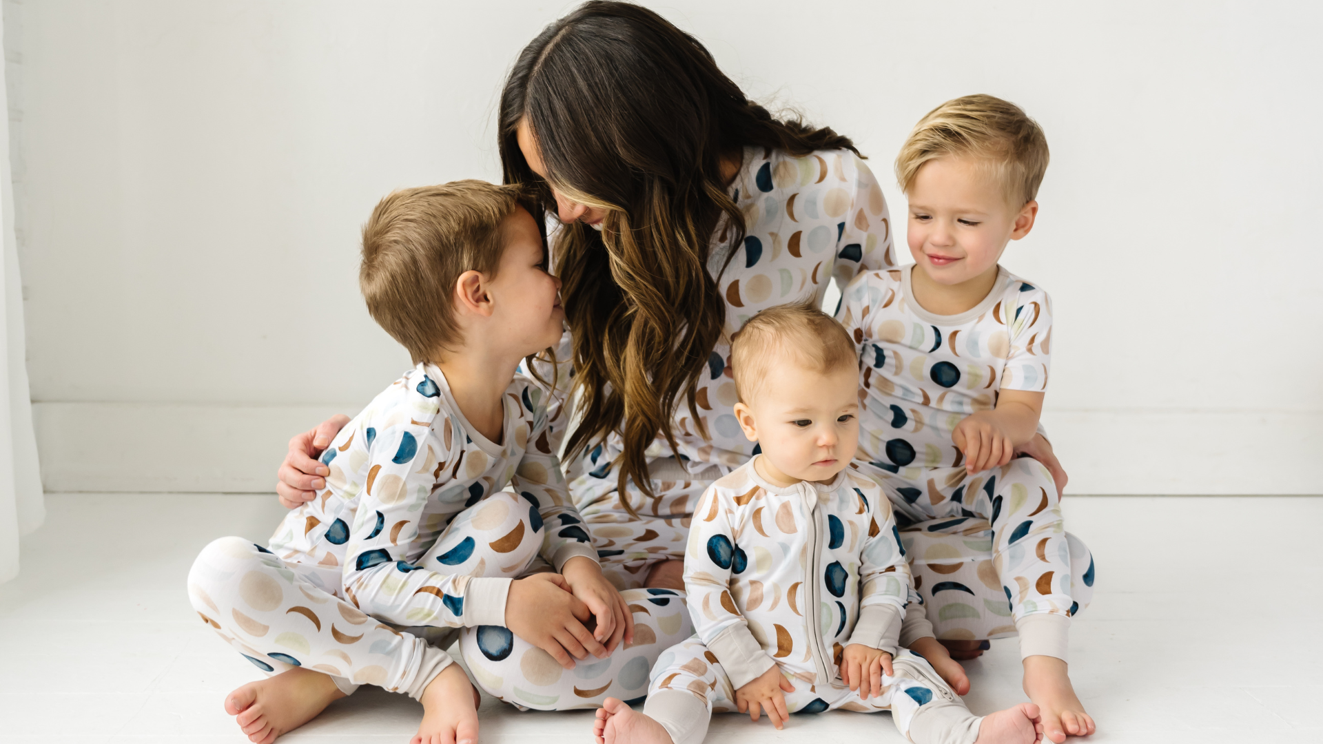 family of four sitting on the ground wearing matching Luna Neutral pajamas