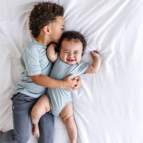 two children laying on a blanket wearing matching play clothes by little sleepies