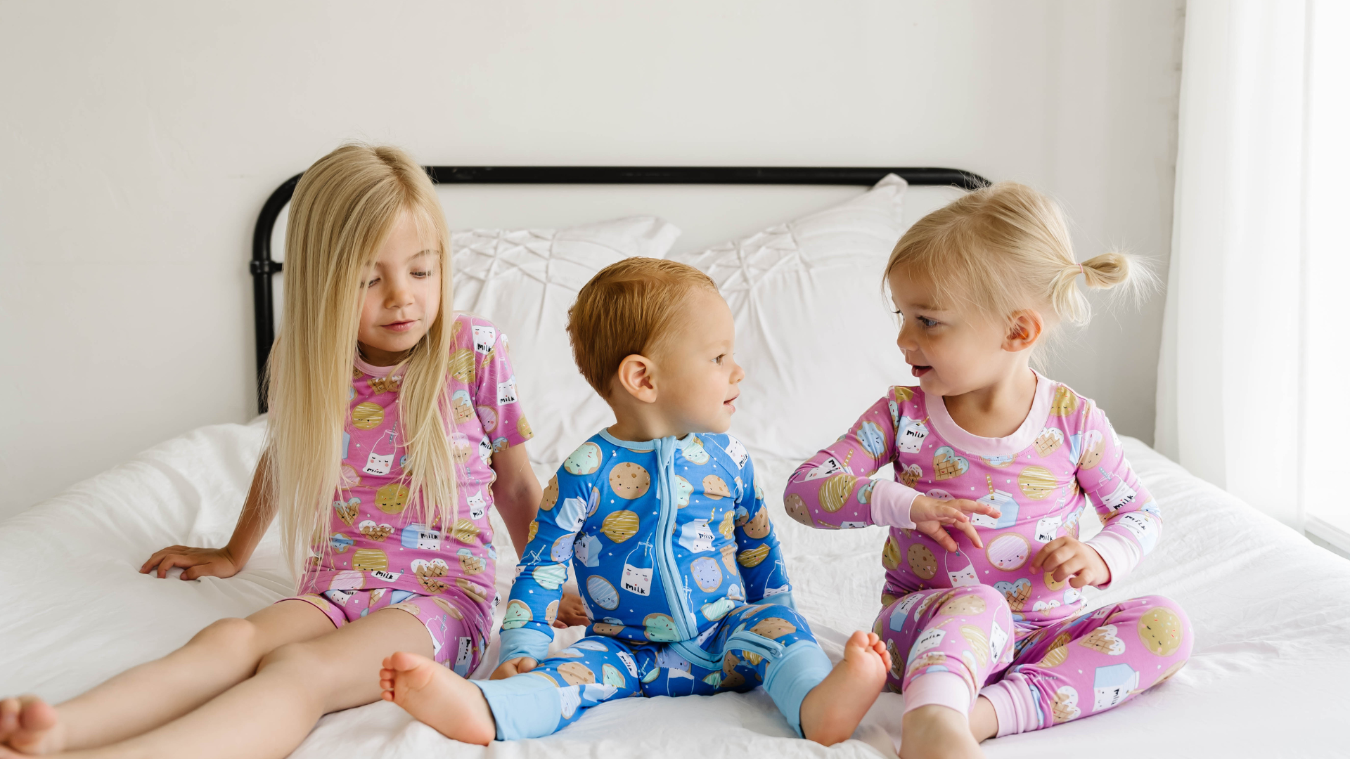 three children sitting on a bed wearing matching cookies & milk pajamas