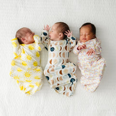 three babies wearing Sunshine, Luna Neutral, and Pastel Rainbow Infant Gowns