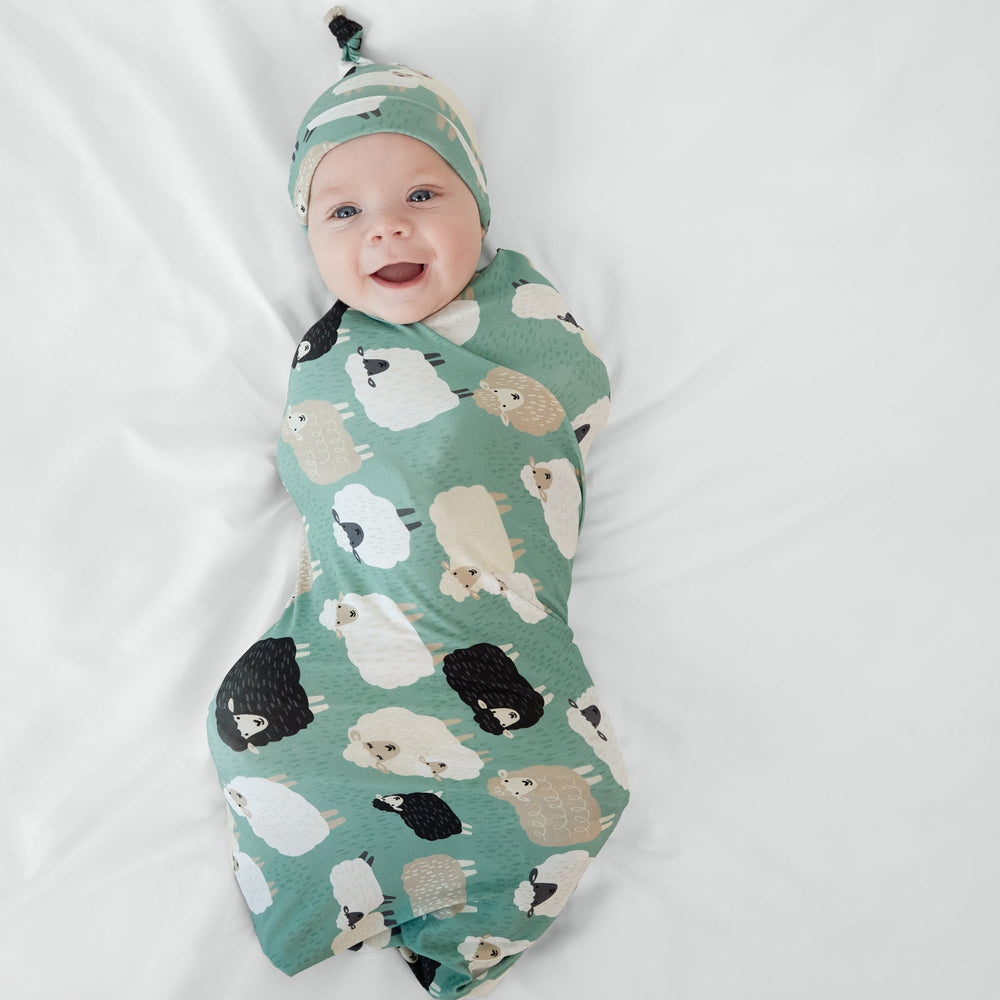 Child wearing the Little Sheepies swaddle and hat set