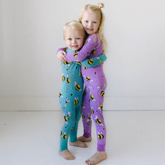 A small boy and a girl hugging dressed in coordinating teal and purple pajamas featuring black and yellow bees on the print.