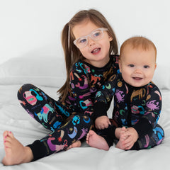 Two children sitting together wearing the Star Signs two-piece long sleeve pajama set and the Star Signs zippy