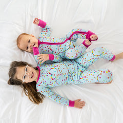 two children laying in bed wearing a friends forever two-piece pajama set and a friends forever zippy