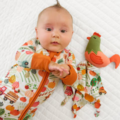 Child laying on a bed wearing a Happy Harvest Zippy and matching Rooster Sleepyhead Lovey