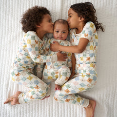 Three children laying on a blanket wearing matching Check Mates pajamas