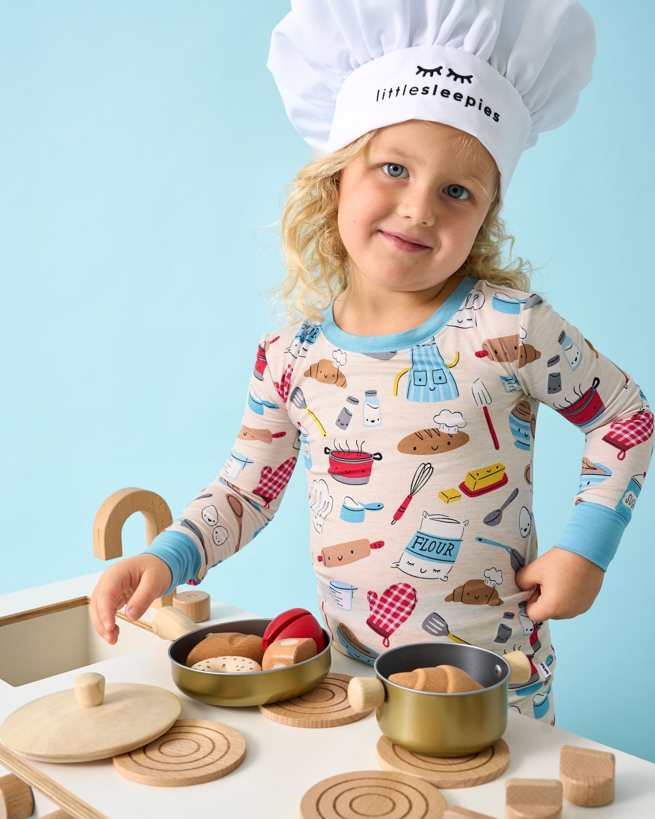 Girl playing with a wooden kitchen wearing the Little Chef pajamas 