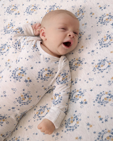 Baby wearing a Lullaby Sky zippy on a matching crib sheet
