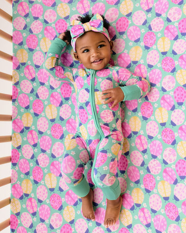 Aerial view of baby wearing the Ladybug Meadow Zippy on a matching crib sheet