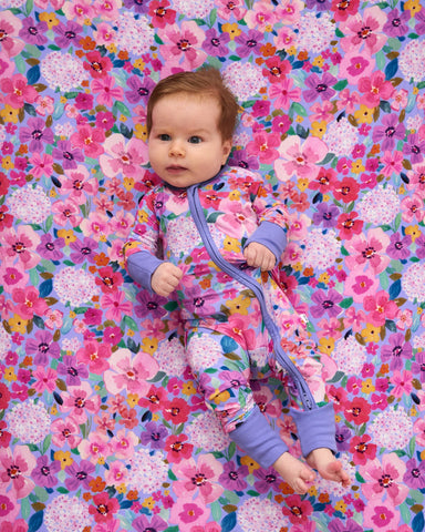 Aerial view of baby wearing the Sweet Sprigs footie on a matching floral crib sheet