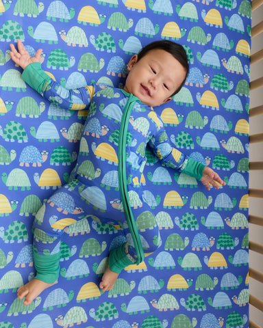 Aerial view of baby wearing the Shell Parade zippy on a matching crib sheet