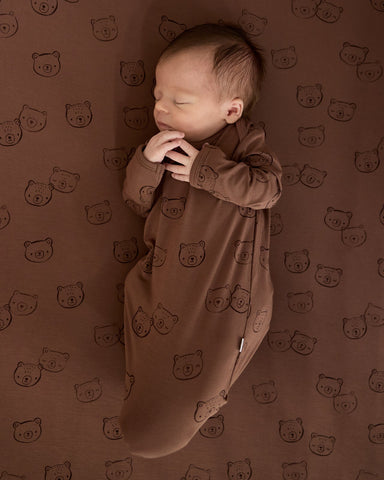 Baby wearing a Teddy Tracks infant gown on a matching crib sheet 