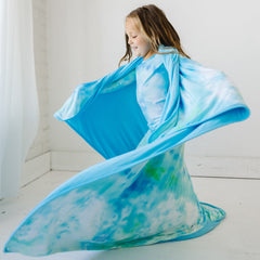 child twirling wearing a Tidepool Watercolor blanket over her shoulders