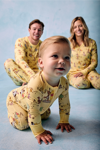 Family of three wearing matching Playtime With Pooh pajamas