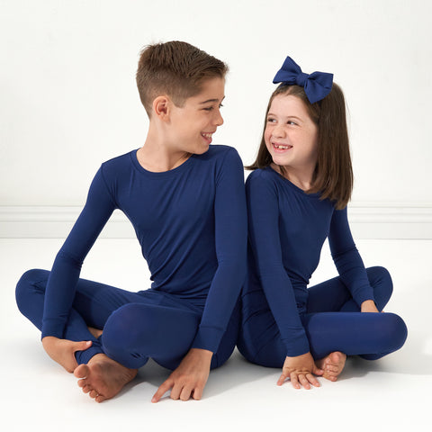 two children wearing Sapphire solid two piece pajama sets paired with a luxe bow headband