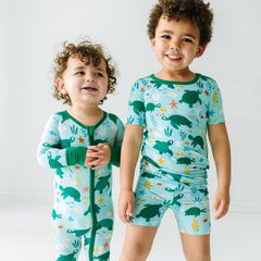 two children wearing sea turtle friends printed pajamas in zippy and short sleeve and shorts styles.