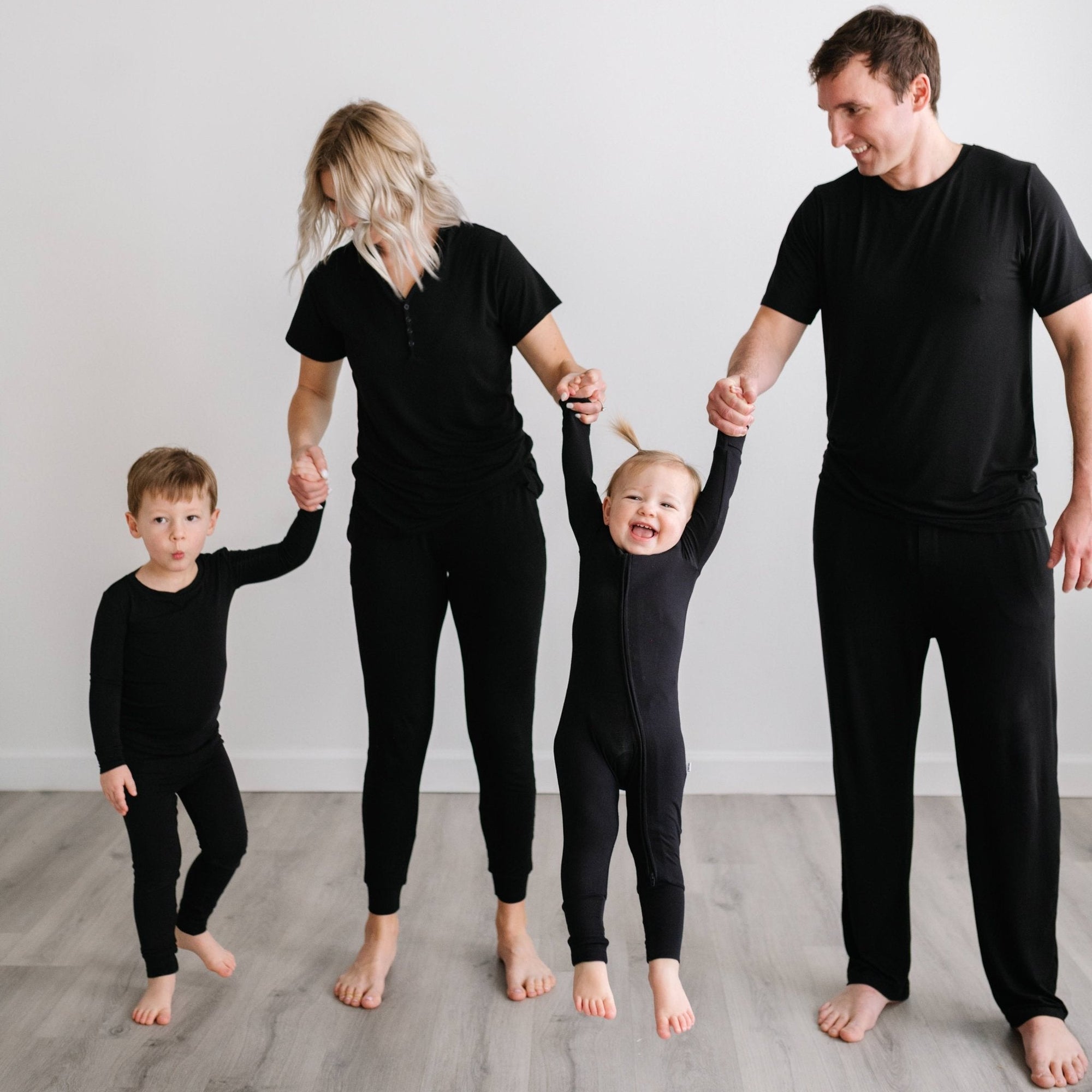 family of four holding hands wearing matching black pjs
