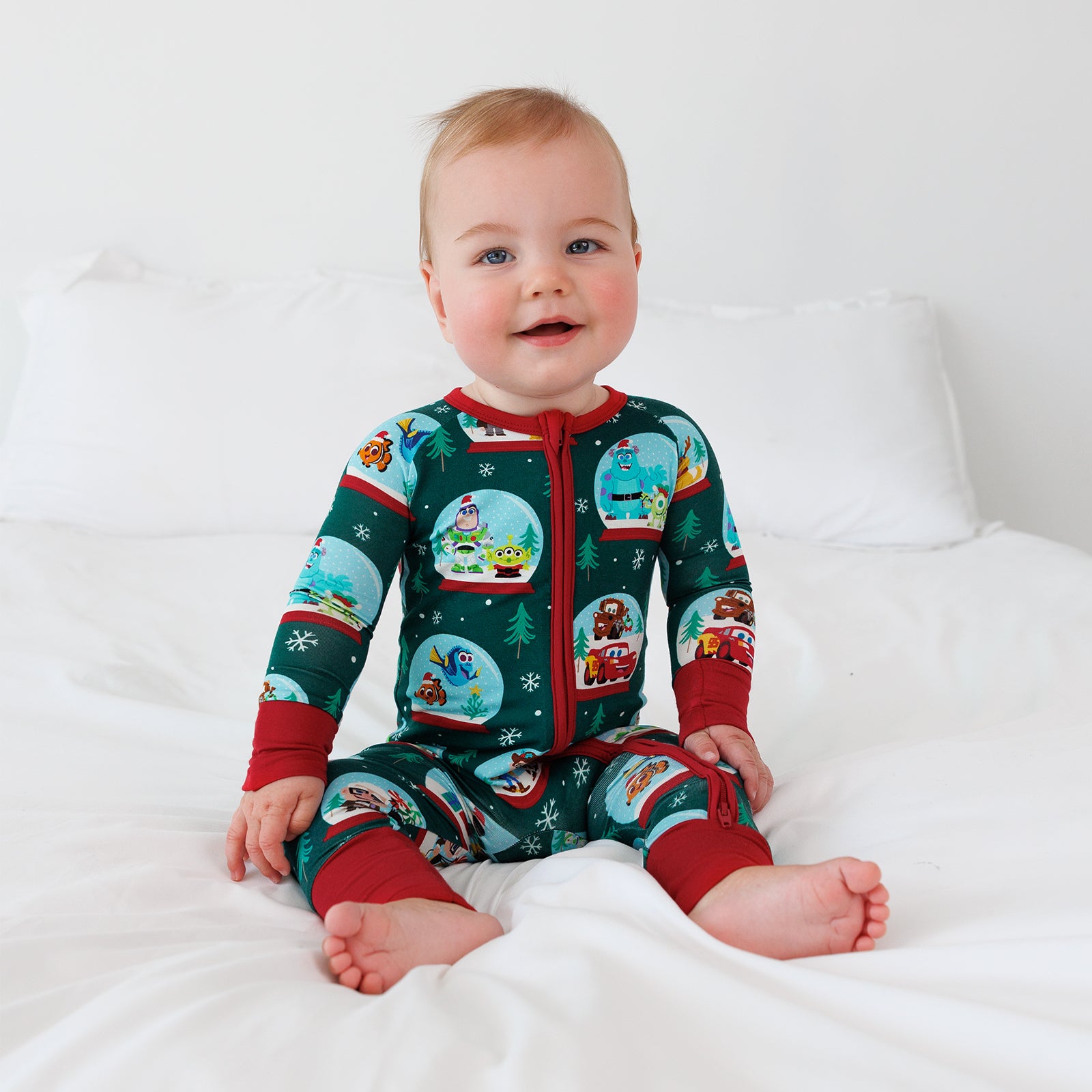 Baby sitting on a white bed while wearing the Disney A Very Pixar Christmas Zippy