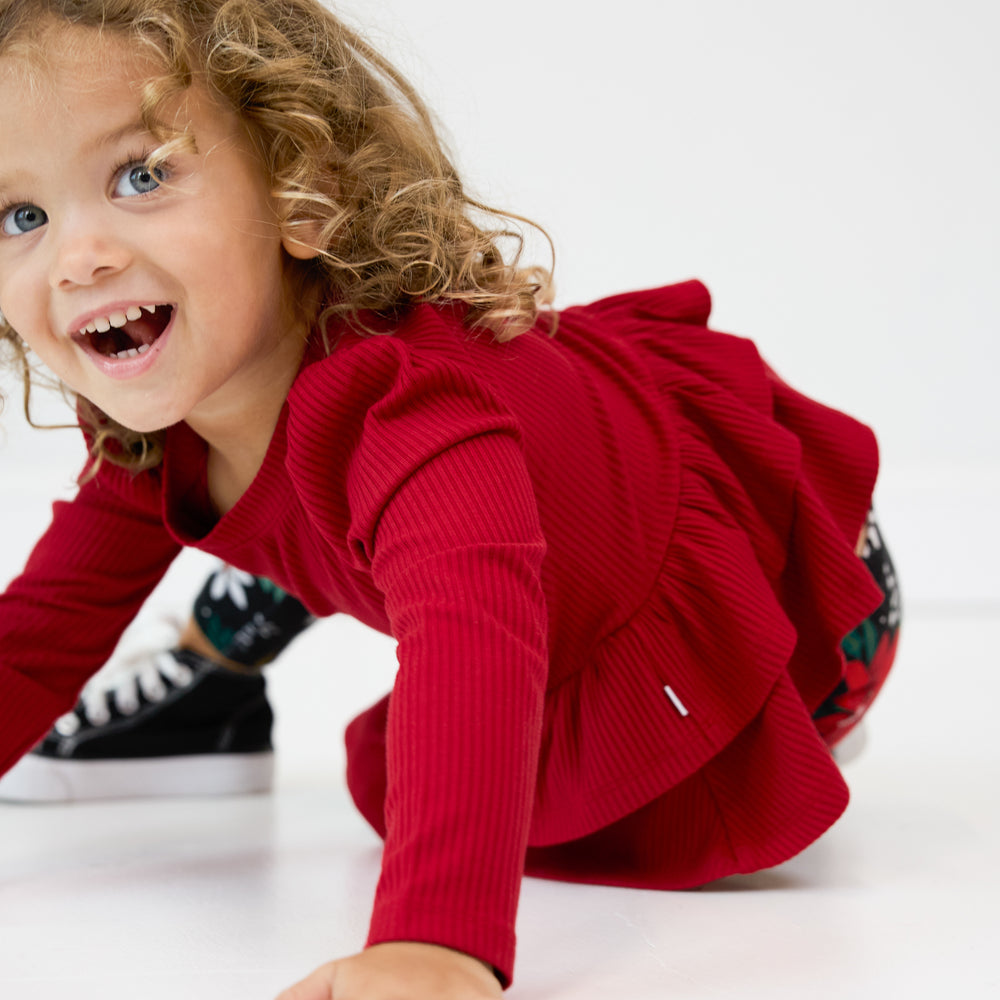 Close up image of a child sitting on the ground wearing a Holiday Red Ribbed Tiered Peplum Top