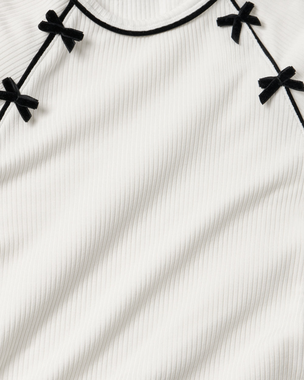 Close-up of a white ribbed knit top with black trim and small black bow details along the neckline.