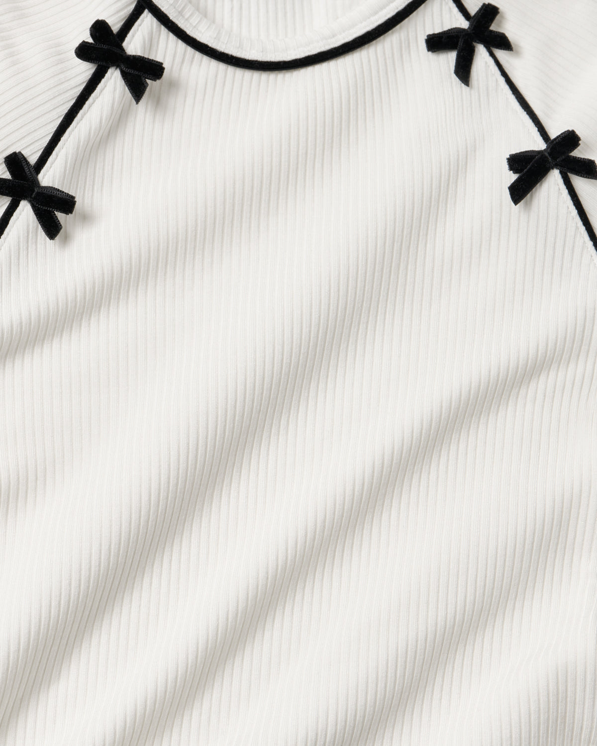 Close-up of a white ribbed knit top with black trim and small black bow details along the neckline.