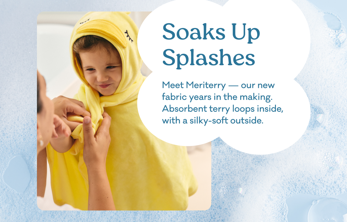 A child wearing a yellow hooded towel wrap with a face patch, being helped by an adult, set against a light blue bubbly background with text reading 'Soaks Up Splashes. A fabric years in the making, with soft terry loops inside and a silky-smooth outside. Absorbent from hood to hem.'