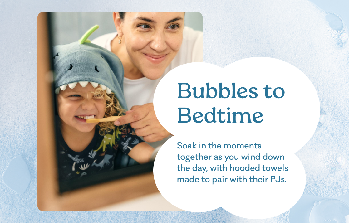 Promotional graphic featuring a woman and child smiling, with the child wearing a blue shark hooded towel. The image has a light blue bubbly background and white text bubbles reading "Bubbles to bedtime. Soak in the moments together as you wind down the day, with their favorite jammies."