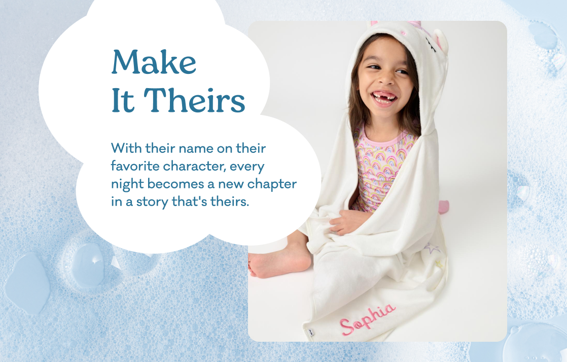 Personalized baby hooded blanket or wrap featuring a smiling young girl wrapped in a white blanket with pink unicorn ears and the name 'Sophia' on the corner. The image is styled as a marketing card with the text 'Make It Theirs. With their name on their favorite character, every night becomes a new chapter in a story that's theirs.'