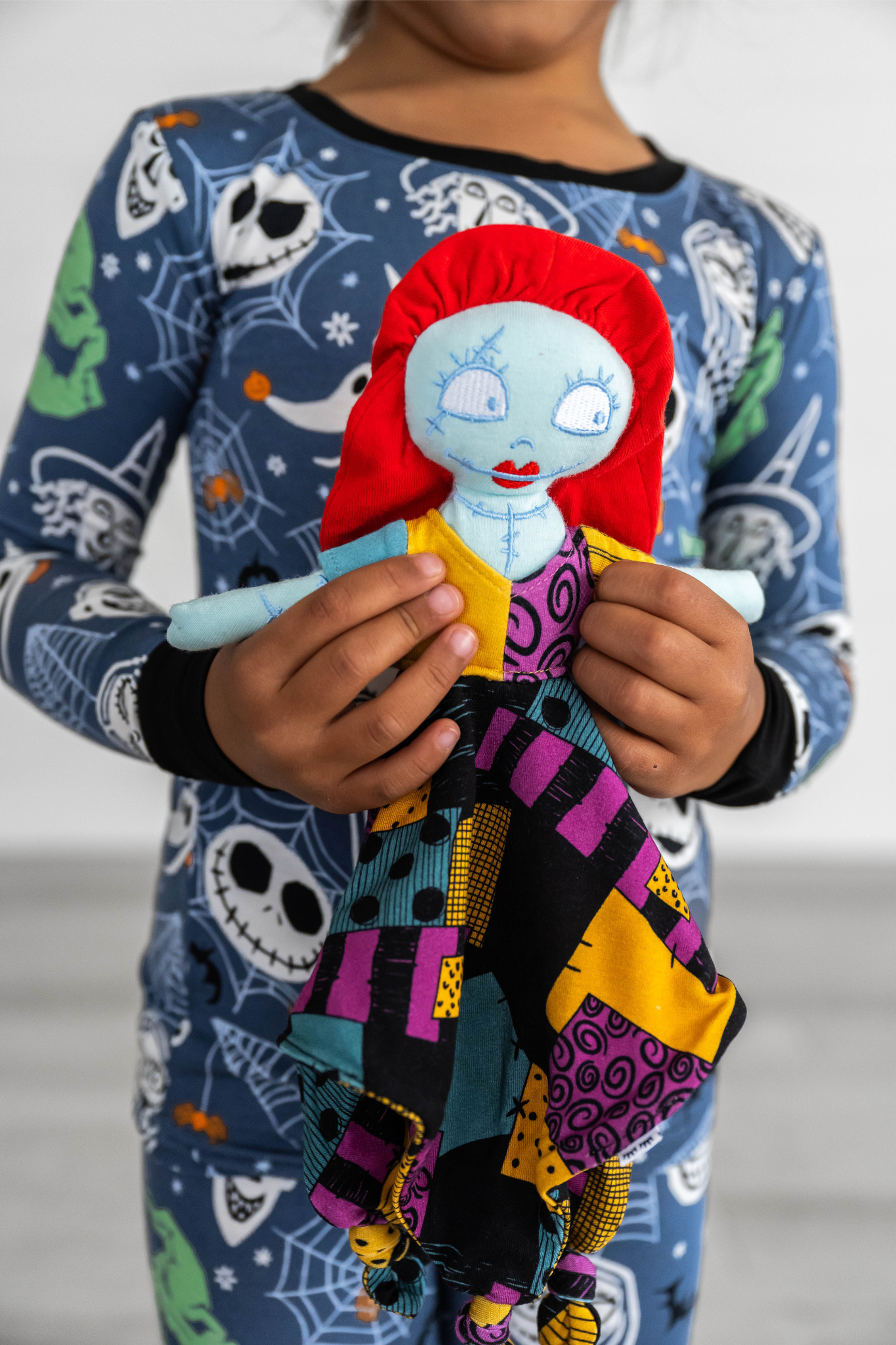 Close-up view of a child wearing nightmare before christmas pajamas and holding a sally lovey