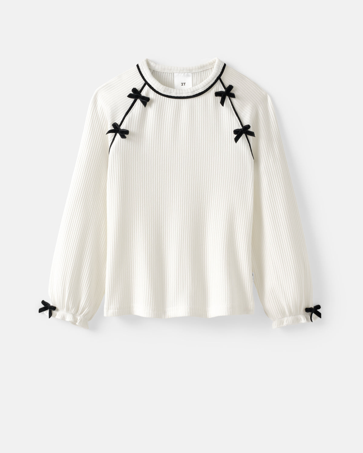 An off-white ribbed long-sleeve blouse with black trim around the crew neck and small black bow details at the shoulders, cuffs, and hem, shown against a light gray background.