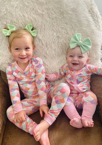 Two sisters wearing matching bamboo pajamas in a two-piece and zippy in Mermaid Scales print by Little Sleepies