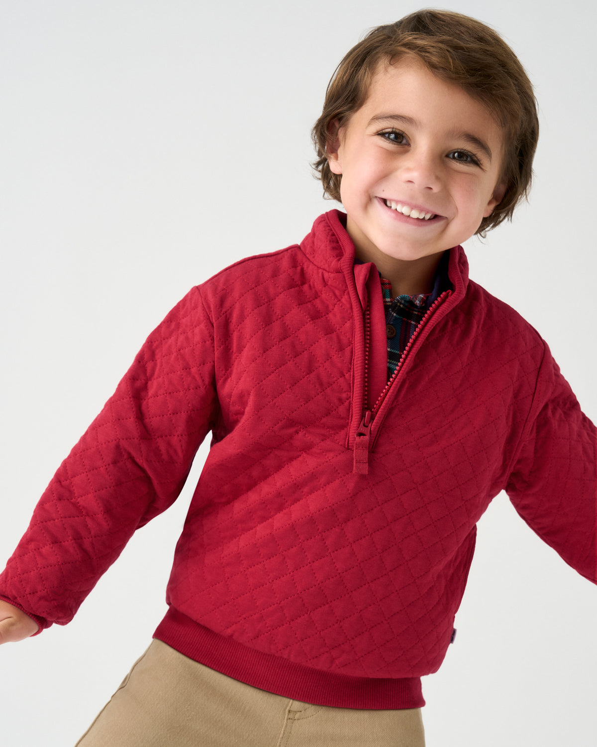 A smiling young boy wearing a red diamond-quilted quarter-zip pullover sweater, paired with khaki pants, photographed against a light gray studio background.