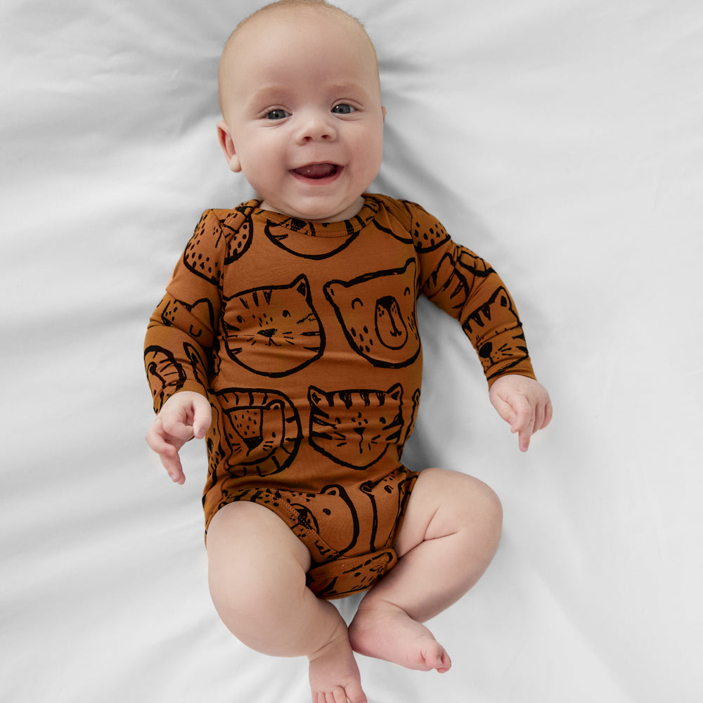 Infant lying on a white blanket wearing an Amber Lions, Tigers & Bears baby bodysuit with black animal illustrations.