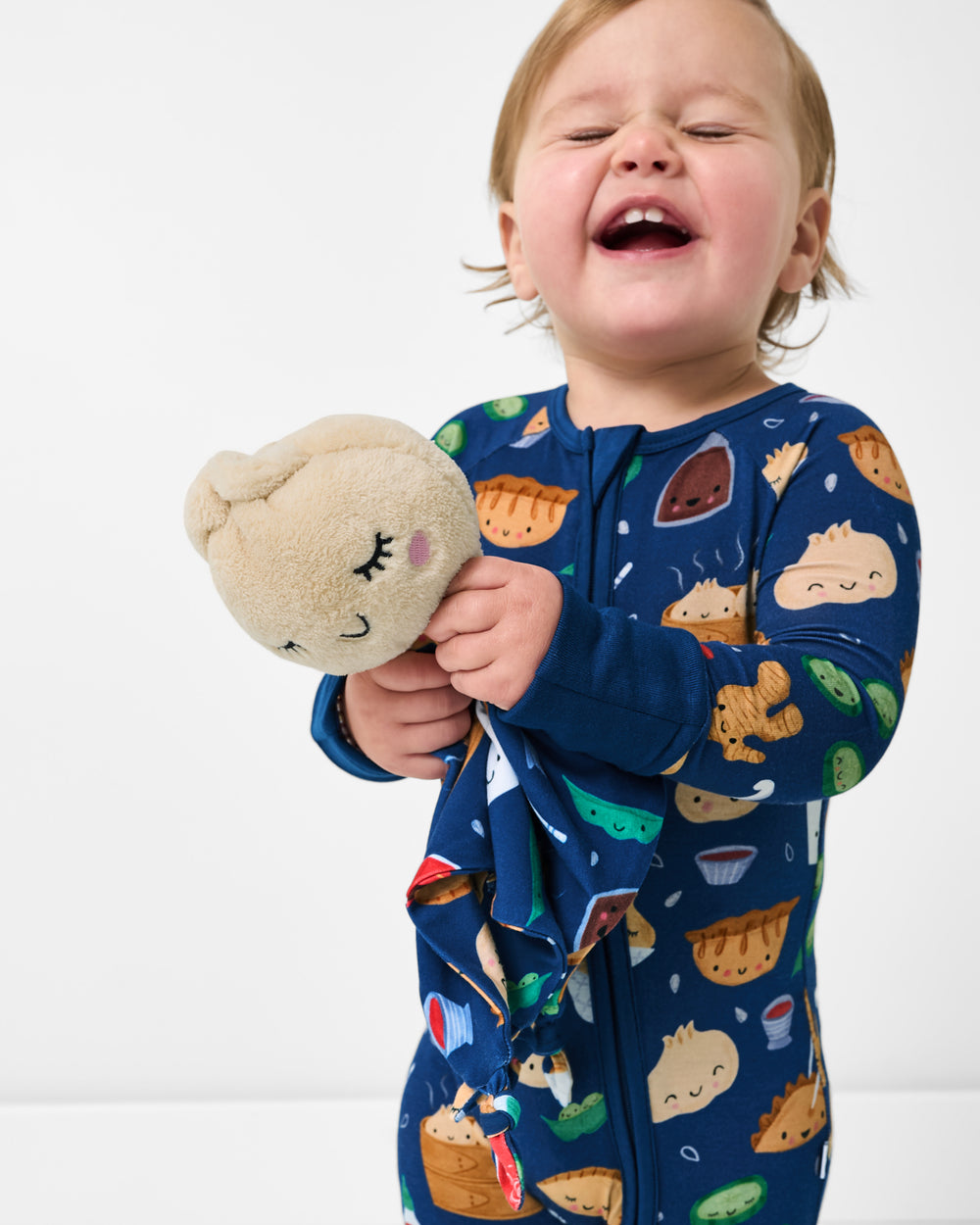 Smiling baby holding the Suki the Dumpling Sleepyhead Lovey