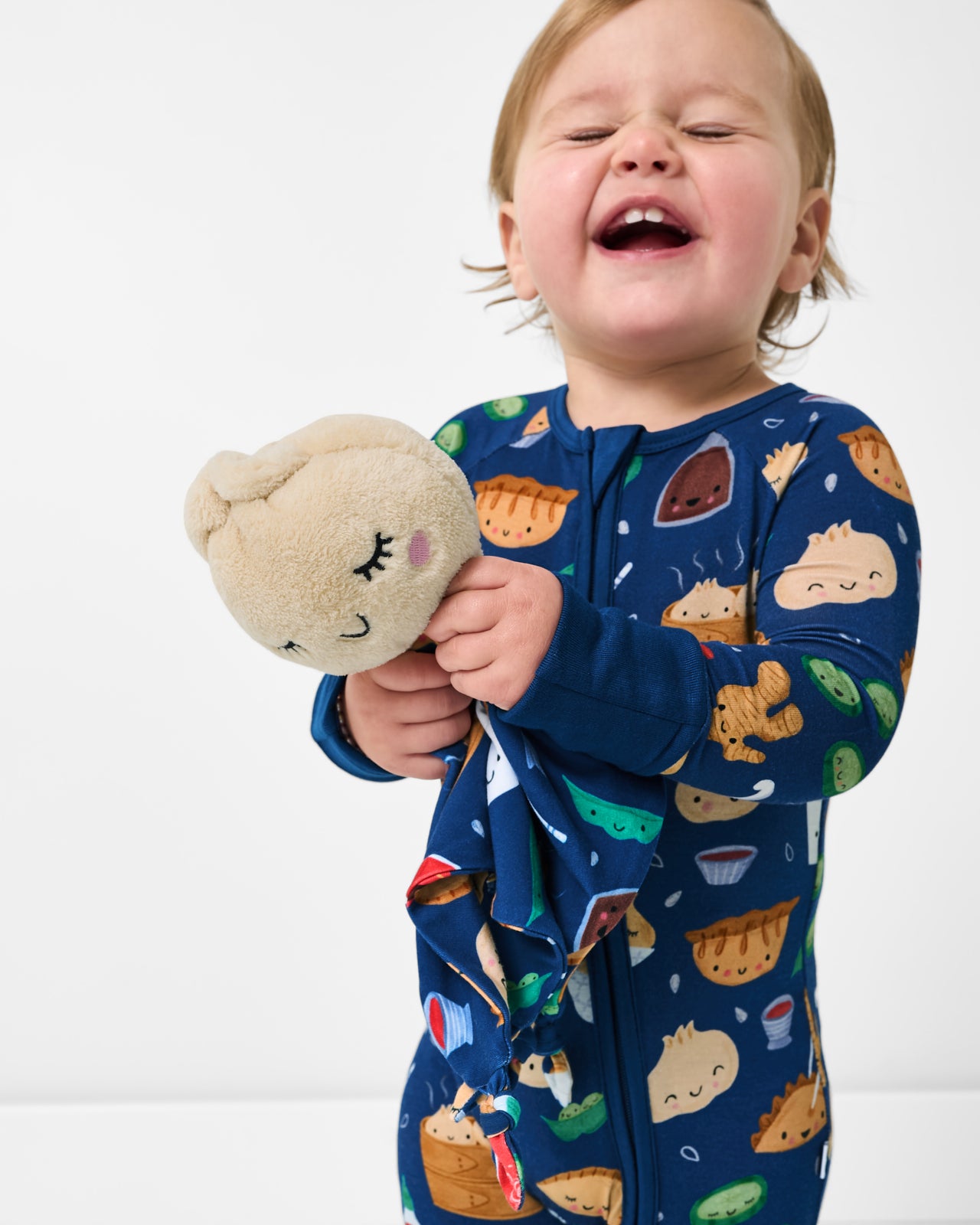 Smiling baby holding the Suki the Dumpling Sleepyhead Lovey