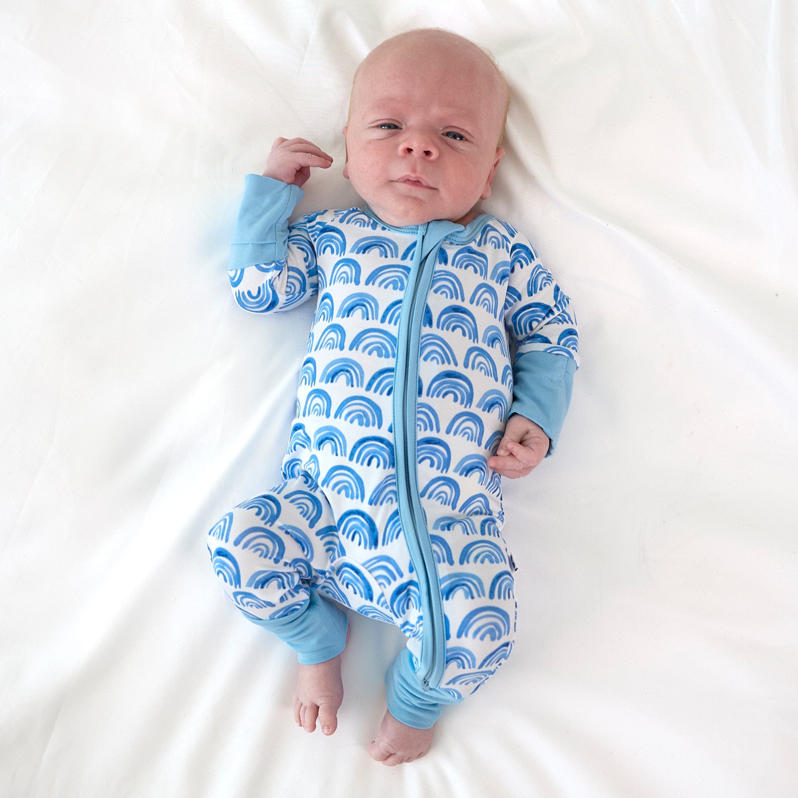 newborn baby wearing the blue rainbows zippy lying on a bed