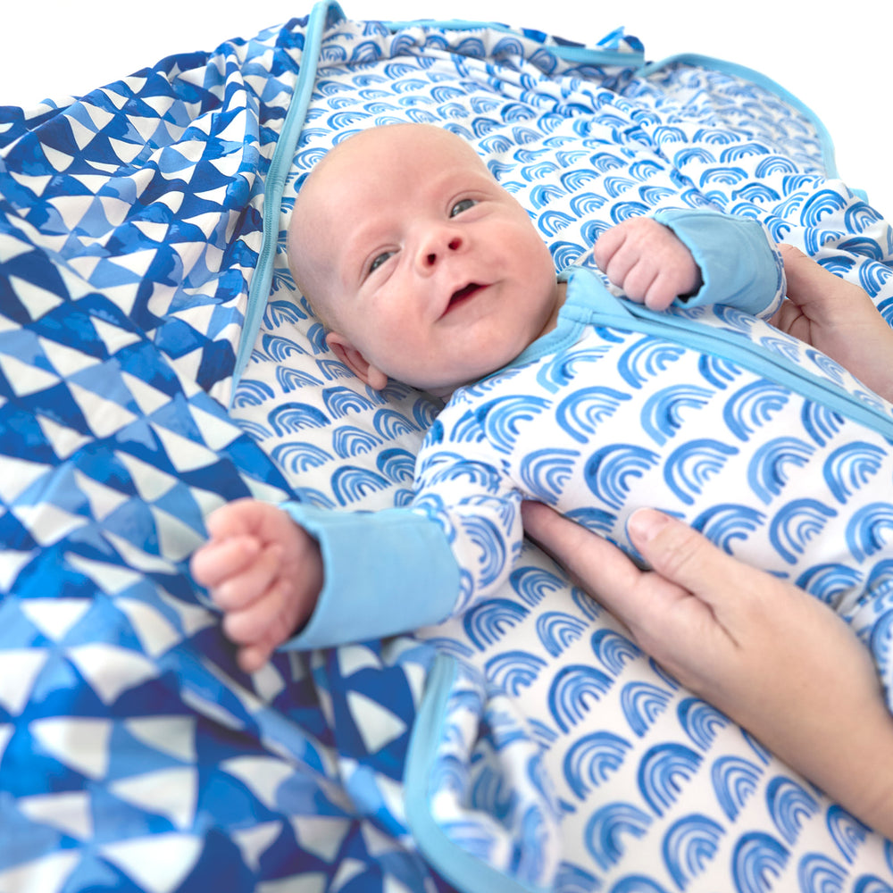 newborn baby lying on the blue rainbows blanket with an adult holding his sides.