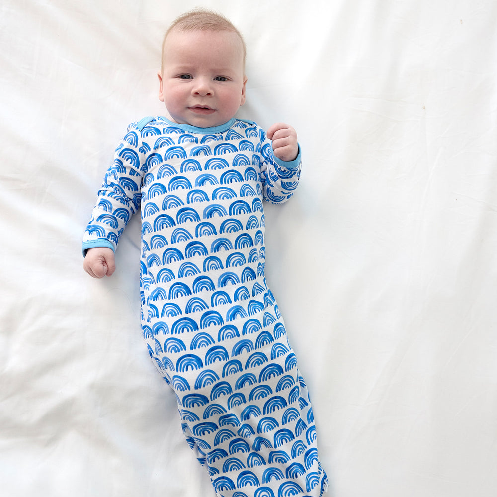 photo of baby in blue rainbows newborn gown lying on bed
