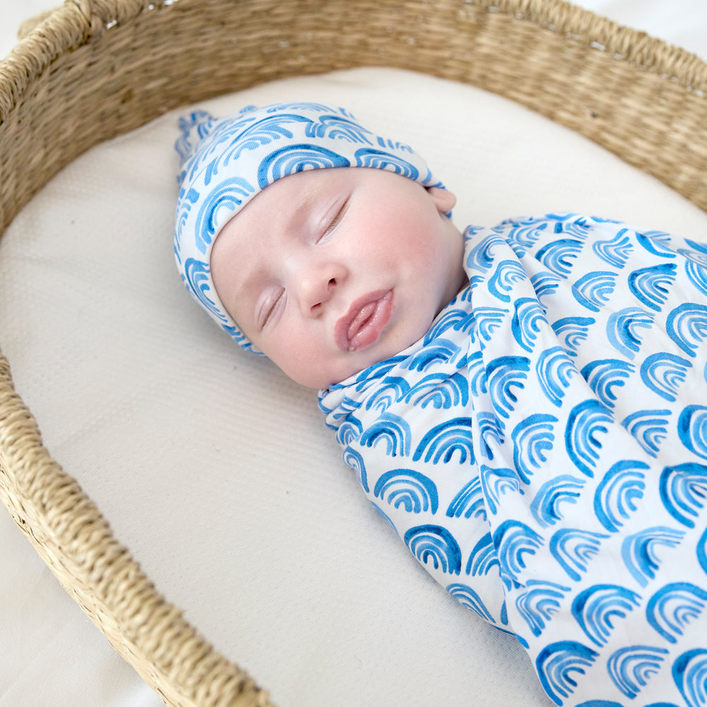 baby in basket sleeping wearing blue rainbows swaddle set with hat close up