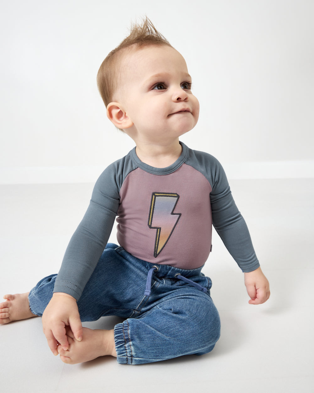 Sitting baby wearing the Bolt Raglan Bodysuit with denim pants