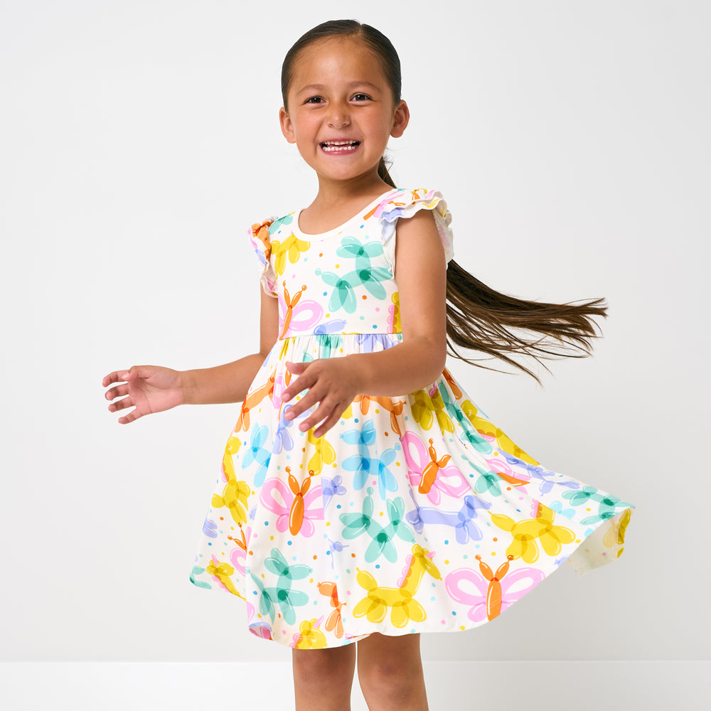 Standing child wearing the Balloon Bash Flutter Twirl Dress